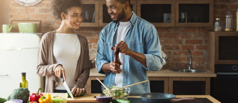 Feliz pareja afroamericana cocinando juntos en la cocina de su loft en casa. Preparando una ensalada de verduras.