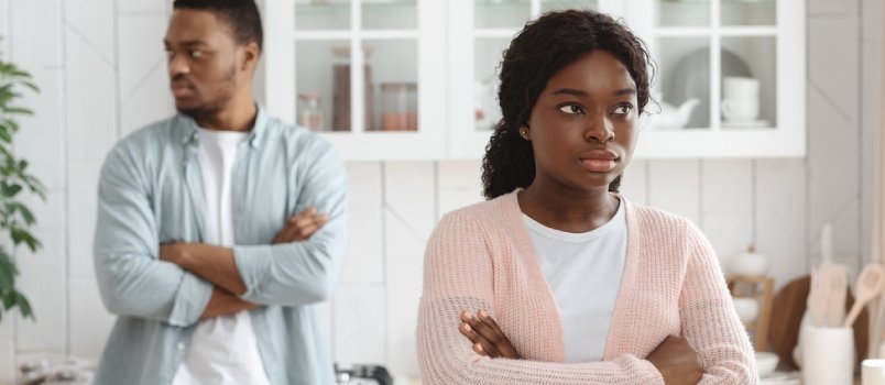 Jóvenes cónyuges afroamericanos que se ignoran mutuamente tras una discusión, hombre y mujer negros ofendidos de pie con los brazos cruzados en la cocina